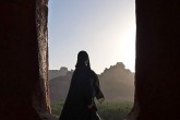 A woman is framed in silhouette against mountains and a bright sky.