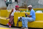 Two friends have a conversation as they sit on a bright, yellow bench.