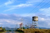 A water tower sits on the side of a road beneath a marble blue sky.