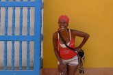 A woman in a red shirt and bandana smiles for the camera as she stands before a vibrant yellow wall.